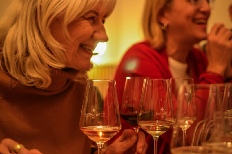 Two women laughing and enjoying wine during a wine-tasting session in Bratislava, surrounded by a selection of wine glasses and snacks on the table