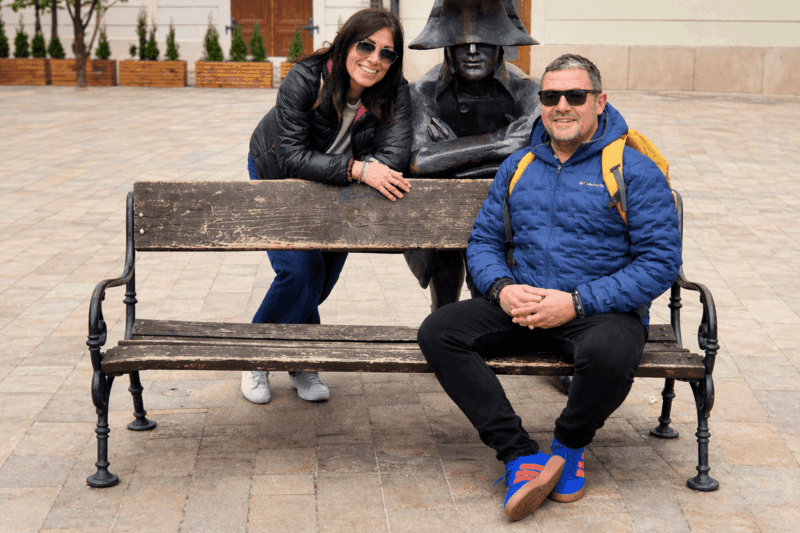 Tourists posing with the Napoleon soldier statue on a bench in Bratislava Old Town during the best day trip from Vienna to Bratislava
