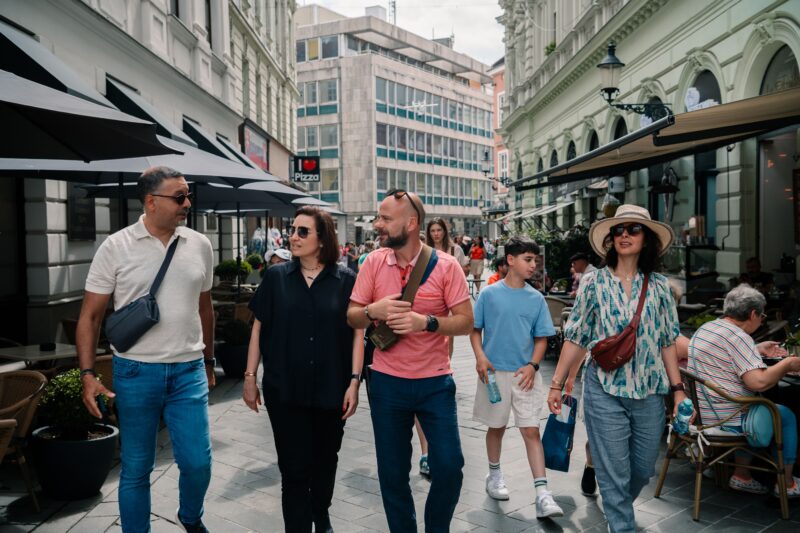 Tourists strolling through the lively streets of Bratislava on a day trip from Vienna. The group enjoys the vibrant atmosphere, passing by cafes and shops in the city center