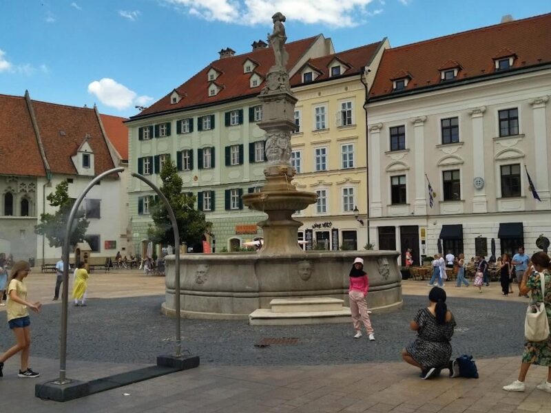 Tourists enjoying a sunny day at the Roland Fountain in Bratislava’s Main Square, with historic buildings in the background