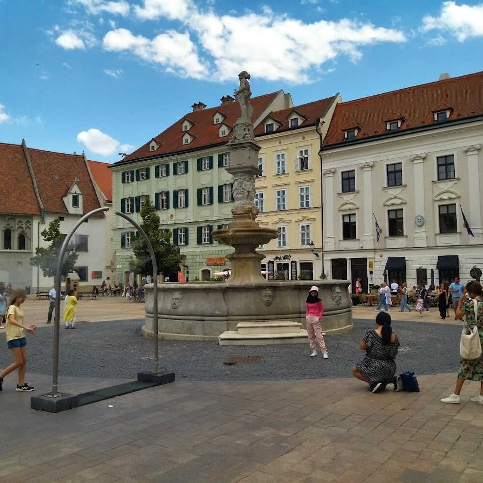 Tourists enjoying a sunny day at the Roland Fountain in Bratislava’s Main Square, with historic buildings in the background