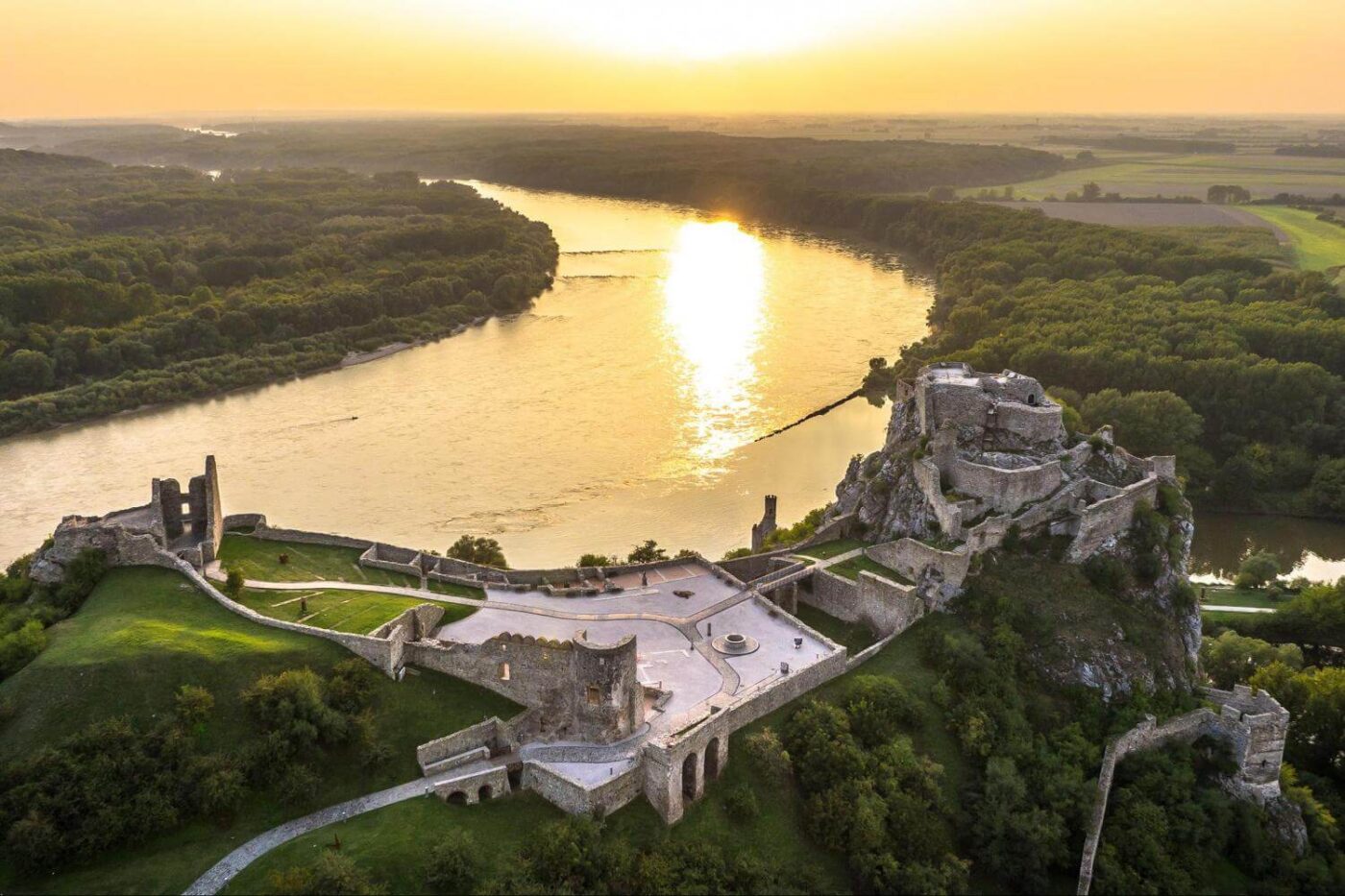 Stunning aerial view of Devin Castle at sunset, overlooking the confluence of the Danube and Morava rivers, an ideal destination for a one day trip from Bratislava to Devin.