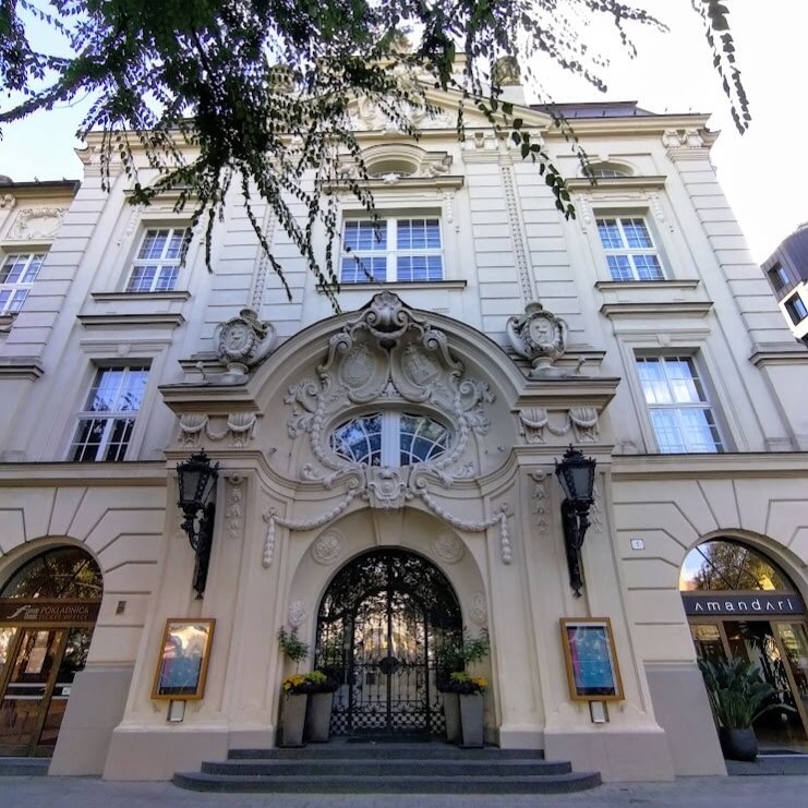 Front view of the Reduta Building in Bratislava, showcasing its ornate Baroque-style architecture with intricate sculptures and an arched entrance framed by two lanterns. The cream-colored facade reflects the historic significance of this cultural venue.