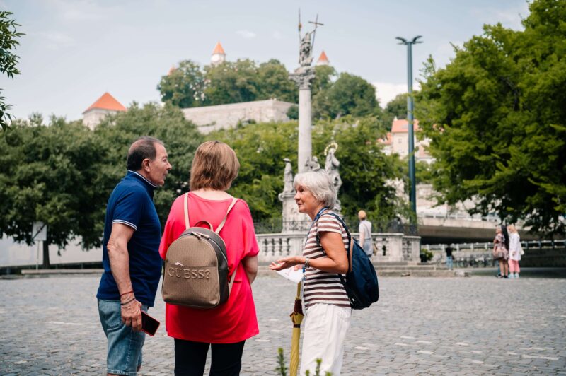 Clients speaking with her guide in Bratislava in front of plague column during their transfer from Vienna to Budapest with Bratislava City Tour