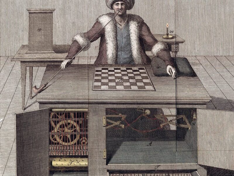 An 18th-century illustration of the Mechanical Turk, a chess-playing automaton created by Wolfgang von Kempelen. The image shows a figure dressed in Ottoman-style attire seated behind a chessboard, with an exposed cabinet below revealing gears and mechanisms. The design was an illusion concealing a human operator who controlled the machine's moves