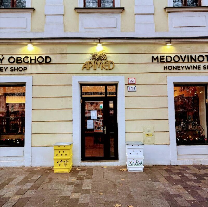 Exterior of Apimed Honeywine Shop in Bratislava, showcasing its welcoming storefront with bee-themed decorations and vibrant yellow beehive boxes outside