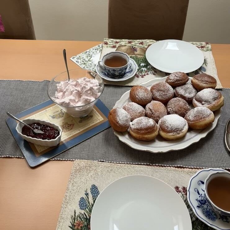 A cozy table setting with a plate of freshly made Šišky, traditional Slovakian donuts, dusted with powdered sugar. Accompanying them are a bowl of whipped fruit cream, a dish of jam, and cups of tea, ready for a delightful homemade trea