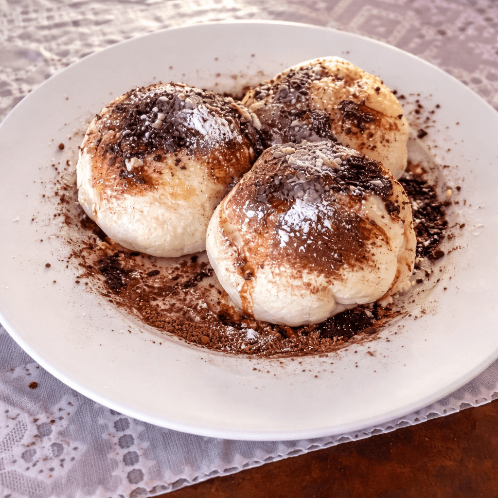 Three fluffy Slovak steamed buns (parené buchty) served on a white plate over a lace tablecloth, generously dusted with ground poppy seeds and powdered sugar — a classic homestyle Slovak dessert, photographed at a traditional countryside setting.