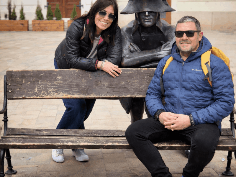 Couple sitting with the Napoleon soldier statue on a bench in Bratislava Old Town — a must-see stop on any Bratislava one day itinerary 2026