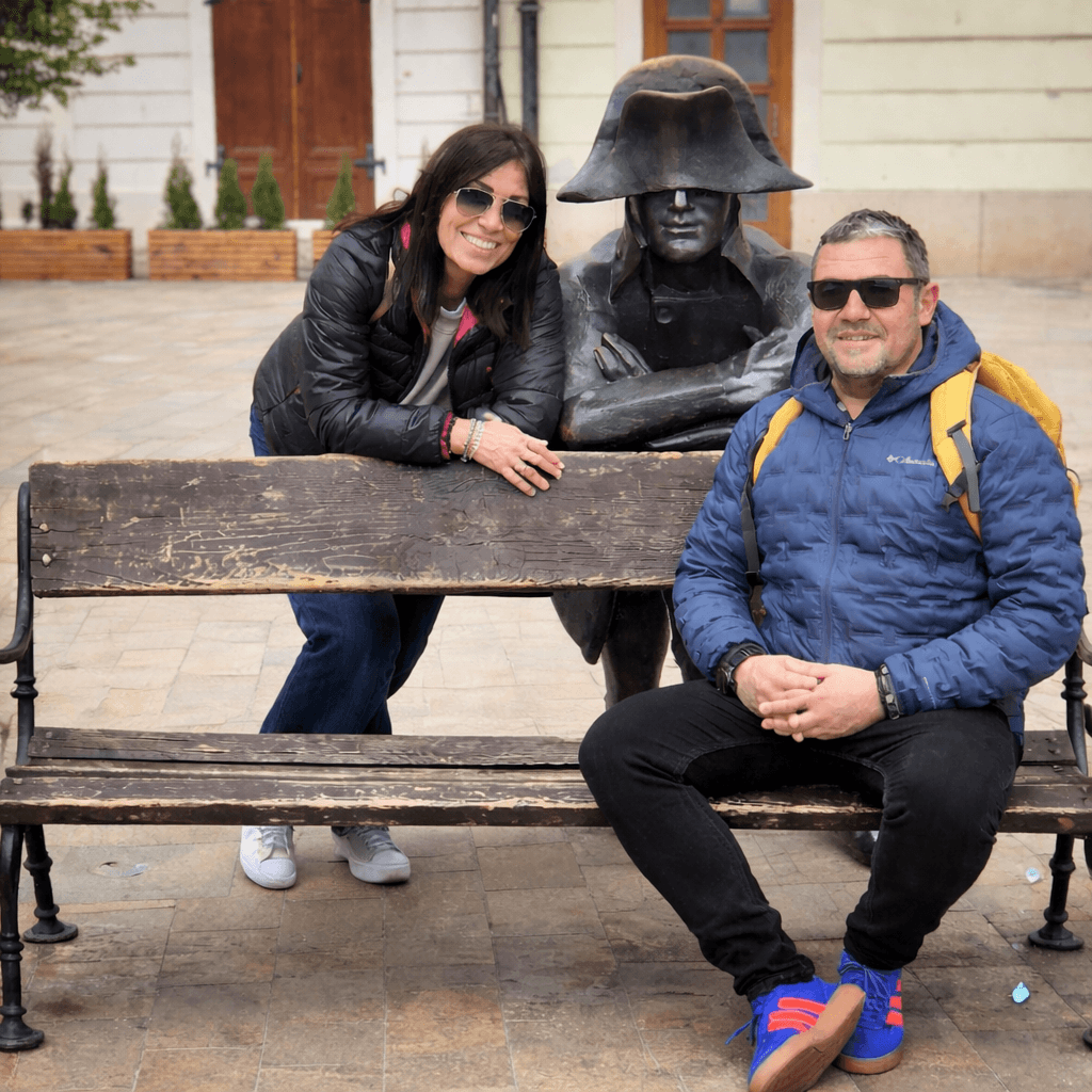 Couple sitting with the Napoleon soldier statue on a bench in Bratislava Old Town — a must-see stop on any Bratislava one day itinerary 2026