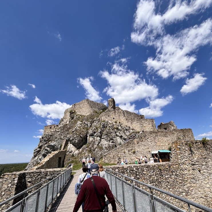 Visitors walking across the bridge towards Devín Castle ruins on a sunny day, a popular half-day trip from Bratislava