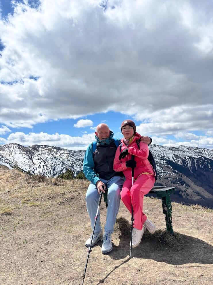 Two hikers resting on a mountain bench with snow-covered Small Fatra peaks in the background — hiking day trip from Bratislava